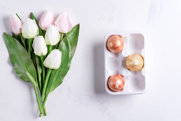 Golden Easter Eggs in ceramic egg tray with pastel tulips on stone marble background. Easter background or easter concept.