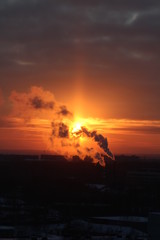 Red sun at sunset or dawn at dusk low above the horizon shrouded in smoke from the chimneys of the plant