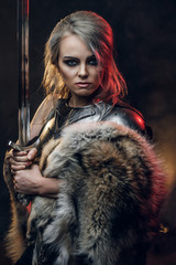 Portrait of a beautiful warrior woman holding a sword wearing steel cuirass and fur. Fantasy...