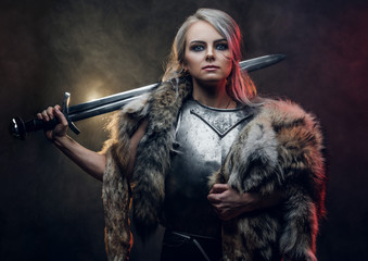 Portrait of a beautiful warrior woman holding a sword wearing steel cuirass and fur. Fantasy...