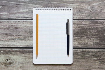 Notepad with a blank white sheet in a checker paper with ball pen and simple graphite pencil lies on the background of wooden boards