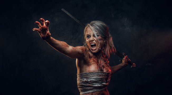 Fantasy woman warrior wearing rag cloth stained with blood and mud holding a sword and rushes into battle with a furious cry. Studio photo on a dark background with smoke. Cosplayer as Ciri from The