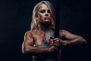 Naked Fantasy woman warrior wearing rag cloth stained with blood and mud posing with a sword....