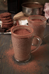 Two cups of hot chocolate with orange Cointreau liquor on a wooden table with oatmeal cookies and chocolate