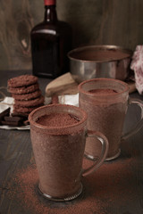 Two cups of hot chocolate with orange Cointreau liquor on a wooden table with oatmeal cookies and chocolate