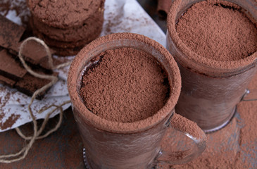 A pair of glass cups of hot chocolate with cinnamon on a wooden table with oatmeal cookies and chocolate