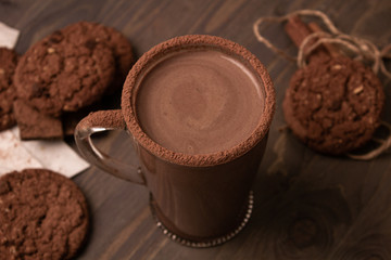 Transparent cup of hot chocolate with cinnamon and milk on a wooden table with oatmeal cookies and chocolate.