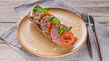 Fototapeta na wymiar Food banner. Mediterranean breakfast or lunch. Bruschetta with salami and tomatoes, cream cheese, pea microgreens and pesto sauce on a ceramic plate