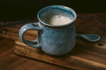 front view of blue rustic cup of coffee with milk on wooden table