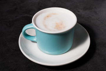 front view of blue cup with plate of coffee with milk on gray background