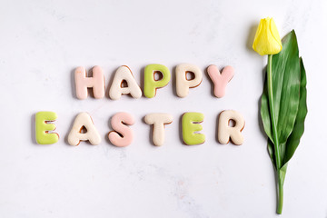 Happy Easter background, Lettering from cookies and yellow tulip on marble background.
