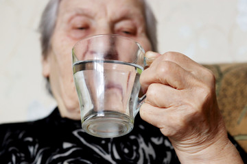 Elderly woman drinking clean water, glass in female hands close-up, selective focus. Concept of thirst, water purification, health care