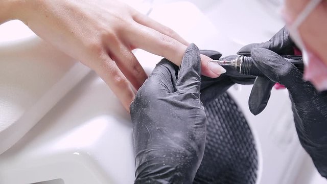 Woman manicurist with gloves in a beauty salon does a hardware manicure to a client before applying a gel coating. translation from blur to sharpen