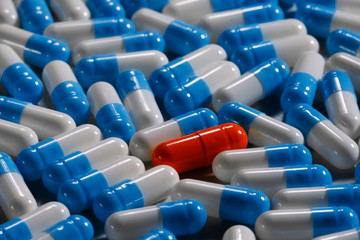 Macro close up shot of a lonely red capsule surrounded by different blue white kind of medicines. Loneliness concept