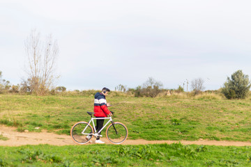 Obraz premium Handsome hipster young man enjoying a bicycle ride and using a smartphone while walking on park