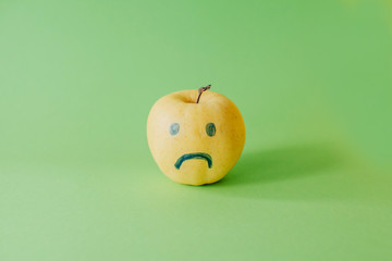 Yellow apple with emotions. Concept of hypocrisy.