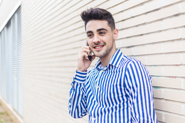 Portrait of handsome young man standing outdoors while using his mobile in the street.