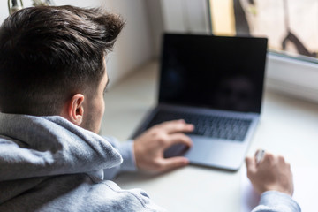 Rear view of a young man working with laptop on desktop at home