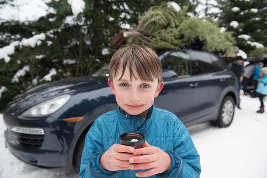 A boy holds a cup of hot chocolate after cutting a Christmas tree.