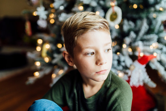 Young boy looking out window next to Christmas tree