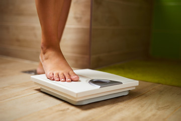 Woman weighing herself on weight scale in bathroom - 322630408