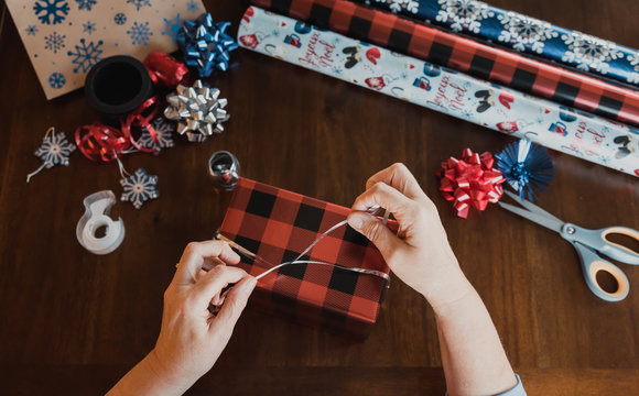 Hands wrapping present at wooden table with gift wrapping supplies.