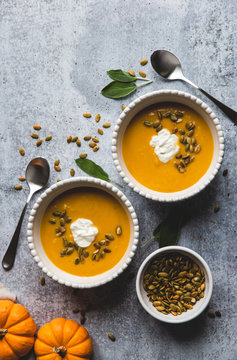 Top view of bowls of butternut squash soup on grey background.