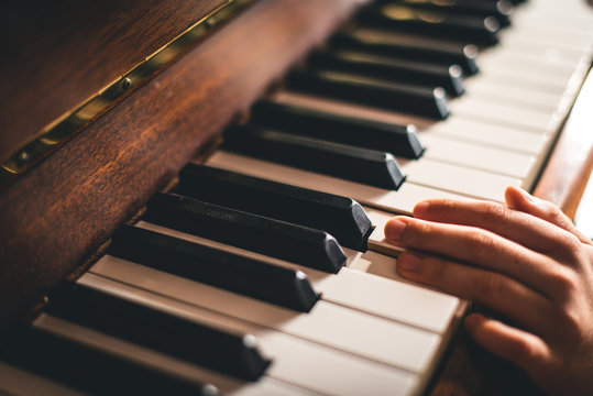 Close up of fingers of a child's hand resting on piano keys.