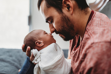 Olive-skinned dad with beard touches nose to swaddled newborn