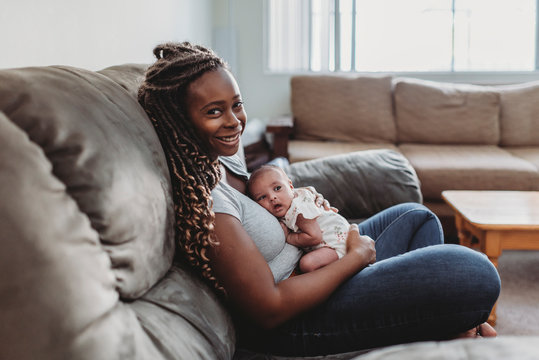 Mid-30?s ethnic mom with long braids on couch holding multiracial baby