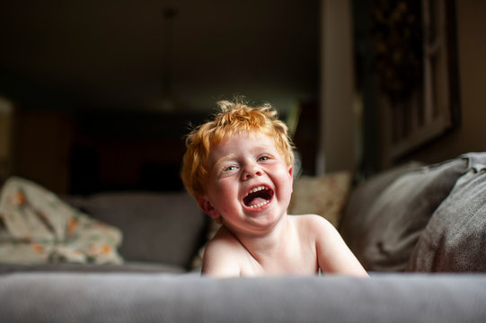 Toddler boy with red hair laughing while laying on couch at home