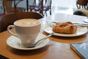 A cup with cappuccino and cookies on a plate on a table with a wooden surface. Breakfast at the cafe. Coffee break.