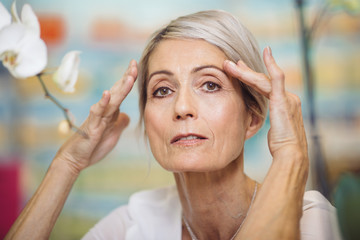 Portrait of 67 year old woman holding her hands near eyebrows