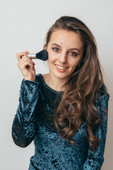 Beautiful young woman in shiny green dress applying powder with a brush to the face.