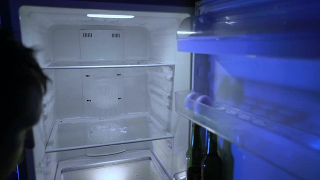 Man looking for food in the fridge. The guy in search of something edible on the empty fridge shelves. Take beer from the fridge. Night hunger. Hangover. Bachelor's fridge, view from behind. 