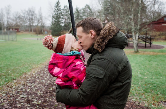 father kissing his daughter whilst playing outside in a park