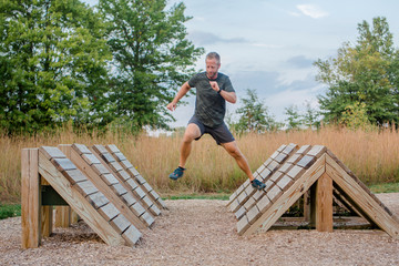An fit man runs across wooden platforms in outdoor obstacle course