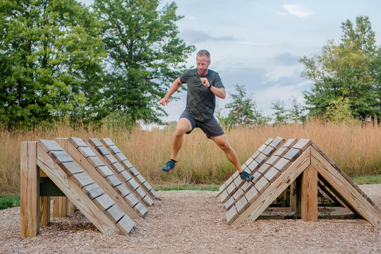 An Fit Man Runs Across Wooden Platforms In Outdoor Obstacle Course