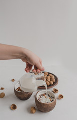 A young woman pours milk into a bowl with granola. A hand holds a creamer, a jug of milk. A healthy...