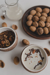 A healthy breakfast of granola, oatmeal, cereals, nuts and milk. Cups with granola, a jug of milk, a plate with nuts on a white background.