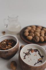A healthy breakfast of granola, oatmeal, cereals, nuts and milk. Cups with granola, a jug of milk, a plate with nuts on a white background.