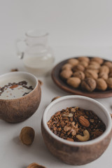 A healthy breakfast of granola, oatmeal, cereals, nuts and milk. Cups with granola, a jug of milk, a plate with nuts on a white background.
