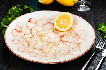 Octopus carpaccio with lemon on white plate.