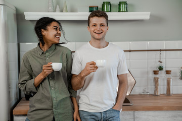 Obraz premium Mixed race couple. International friendship, happy time together, friends having relax time. Enjoy communication and holiday. Happy teenagers girl and guy laughing, drinking coffee on kitchen at home