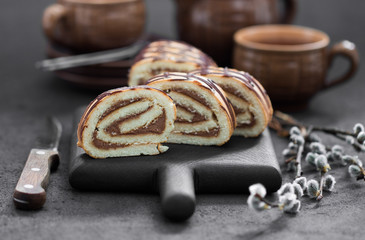 Biscuit cake roll with caramel cream and chocolate on a dark gray background