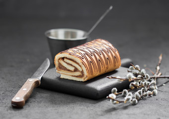 Biscuit cake roll with caramel cream and chocolate on a dark gray background