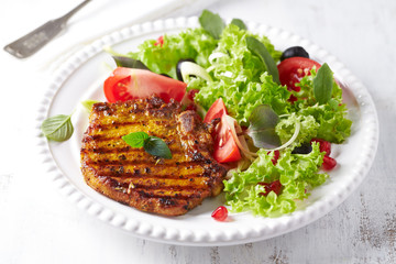 Grilled pork steak with fresh salad. White wooden background