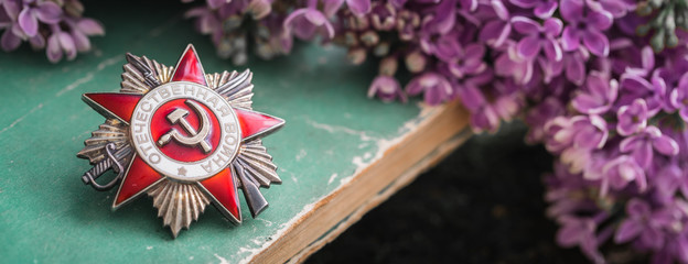 Order, on which is written in Russian - Patriotic War, old books background with lilac, Victory Day...