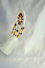 Flying dream catcher in motion, on sky blue background, handmade native american of yellow blue beads with white feathers. Protection from bad dreams, tranquility, freedom, dream, flying, lightness