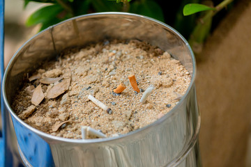 Many cigarette stub in sand ashtray. The rest of cigarettes in the ashtray. There are many types of cigarette stub on the sand in the ashtray. A cigarette is not good for health. 